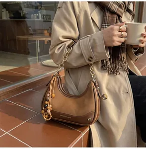 Detail of a brown leather crescent shoulder bag with gold chain and wooden bead tassel