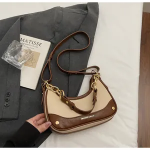 Detail view of contrast leather crossbody bag with decorative gold chain and logo