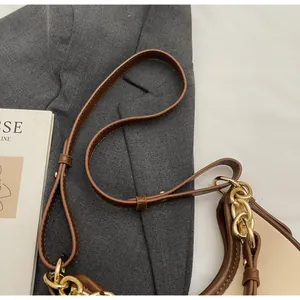 Detail of a brown leather strap with golden chain hardware on a crossbody bag