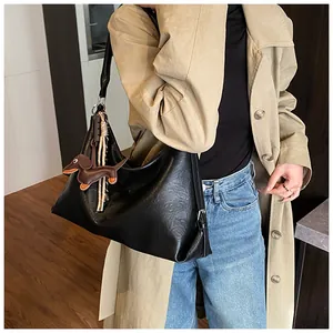 Détail d'un grand sac hobo en cuir noir avec un pendentif teckel marron sur la bandoulière