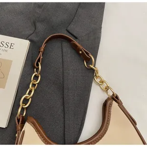 Detail of beige and brown crossbody bag with gold chain strap on grey blazer background