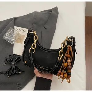 Detail of black leather crescent bag with gold chain strap and wooden bead fringe tassel