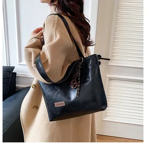 Détail du sac cabas noir avec texture litchi et étiquette mode sur manteau beige