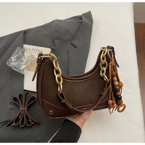 Detail of dark brown leather crescent bag with chunky gold chain and bead tassel