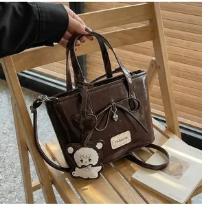 Detailansicht der dunkelbraunen Lederhandtasche mit Schleife und Bärenanhänger-Zubehör