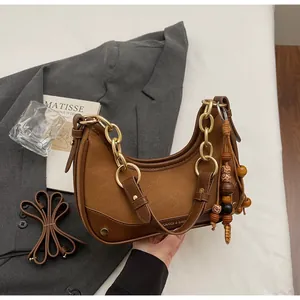 Detail of a brown leather crescent bag featuring a chunky gold chain and beaded accessory