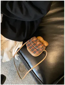 Detail of plaid crossbody bag featuring 3D floral accents and a large brown leather bow