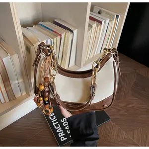 Detail view of contrast color hobo bag with gold chain and wooden bead tassel ornament