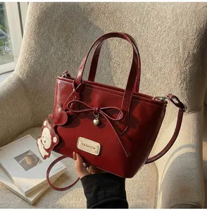 Detailansicht der weinroten Ledertasche mit Schleife, Herzanhänger und kleinem Bärenanhänger