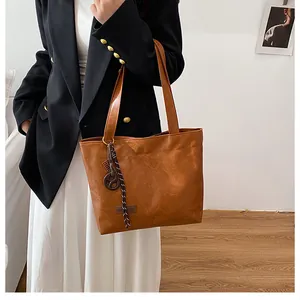 Détail du sac cabas en cuir grainé caramel avec breloque tressée et étiquette mode