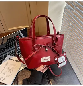 Detailansicht der dunkelroten glänzenden Handtasche mit Schleifendekor und Herzanhänger