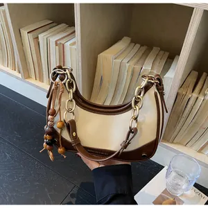 Detail of a chic cream and brown crossbody bag with gold chain and tassel on a bookshelf