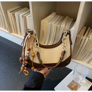 Detail of color-block saddle bag featuring a gold chain handle and wooden bead tassel