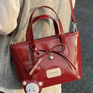 Rote Lackleder-Beuteltasche im Retro-Look mit Schleife und Anhänger am Modell