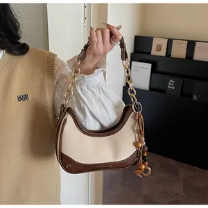 Detail of contrast-color crescent bag with golden chain strap and wooden bead tassel