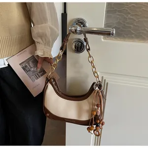 Close-up of contrast hobo bag with gold chain strap and wooden bead tassel detail