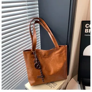 Gros plan sur un cabas en cuir froissé marron avec pendentif anneau sur fond gris