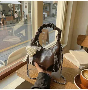 Detail of a dark brown glossy handbag with pleated handles and a pearl heart charm