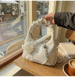 Detail of cream pleated leather handbag with pearl heart charm and silver chain strap