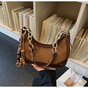 Detail view of brown leather bag with golden chain handle and vintage wooden bead tassel