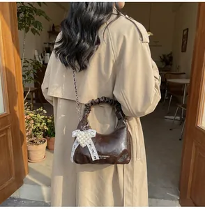 Detailed close-up of shiny dark brown pleated mini bag with pearl heart charm