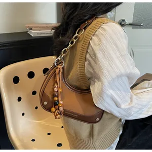 Detail of brown half-moon bag featuring gold chain strap and colorful beaded tassels