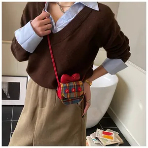 Mini plaid crossbody bag with red bow and floral detail shown on model in a stylish setting