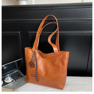 Détail d'un sac cabas marron avec texture cuir, étiquette mode et pendentif tressé