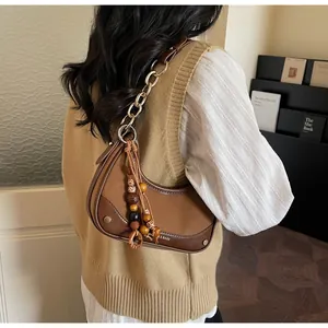 Detail of a brown patchwork half-moon shoulder bag with a stylish metal chain and beaded tassel