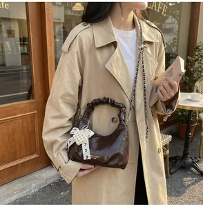 Detail of dark coffee pleated handle handbag with pearl bow charm and silver chain