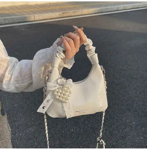Detail of white glossy crescent bag with pleated handle, pearl heart and lace bow