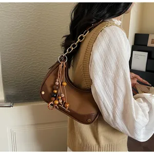 Brown half-moon hobo bag with gold chain and wooden bead tassel shown on shoulder