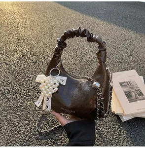 Detail of a dark brown glossy hobo bag with pearl heart charm and silver chain strap