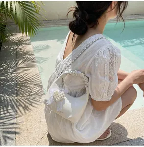 Detail of white pleated handbag with silver chain and pearl heart charm by pool