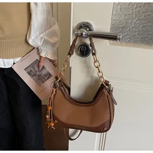 Detail of hobo bag with gold chain strap, wood bead tassel, and brown leather finish