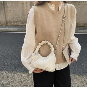 Detail of elegant cream leather handbag with pleated handle and pearl heart charm decor