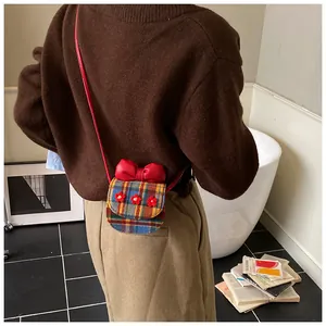 Detail of vintage plaid mini crossbody bag with red bow and flower accents on a model