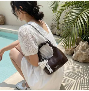 Detail of dark brown glossy hobo bag with pleated handle and pearl bow charm