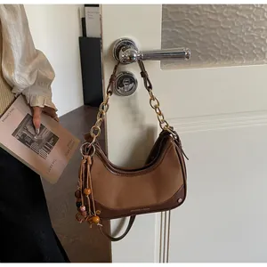 Detail of a brown crescent shoulder bag with gold chain and wooden bead tassel