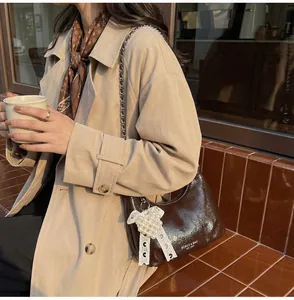Detail of a dark brown patent leather crossbody bag with silver chain and lace bow charm