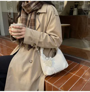 Close-up of white crescent bag with pearl heart charm and lace bow on a trench coat