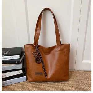 Gros plan d'un cabas marron avec étiquette en cuir, breloque boulier et détails tissés