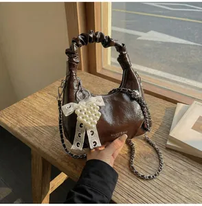 Detail of a brown glossy crescent bag with ruched handle and pearl lace bow charm