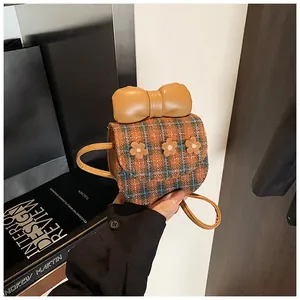 Detail of checkered crossbody bag with orange bow and floral appliques on fabric