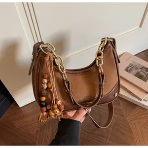Close-up of contrast leather shoulder bag with gold chain and wooden bead tassel