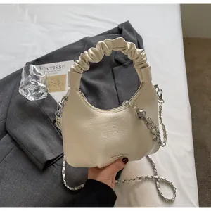 Detail of a creamy white pleated handbag on grey fabric with a silver logo and chain strap