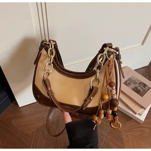 Detail of vintage bicolor leather bag featuring a gold chain and wooden bead tassel
