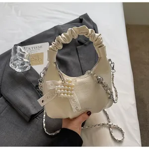 Detail of a creamy white pleated bag on a grey blazer with a silver chain strap