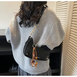 Detail of black leather half-moon bag with gold chain and wooden bead tassel ornament