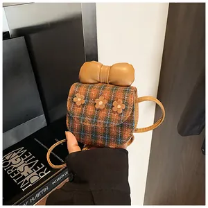 Detailed view of mini plaid crossbody bag with bow and floral accents held by hand